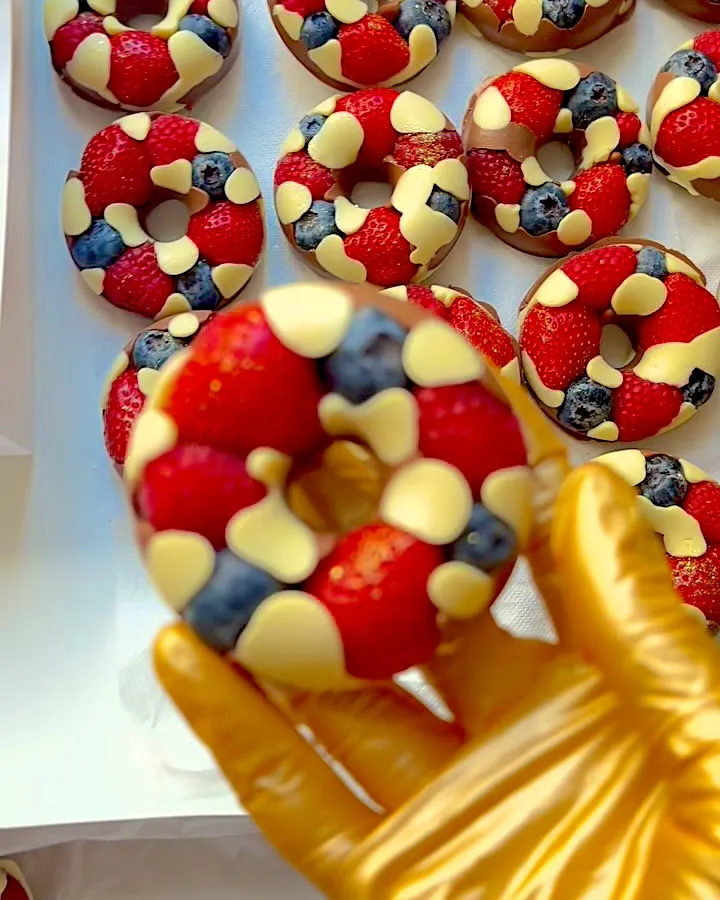 Шоколадные пончики с ягодами, один в руке в золотой перчатке